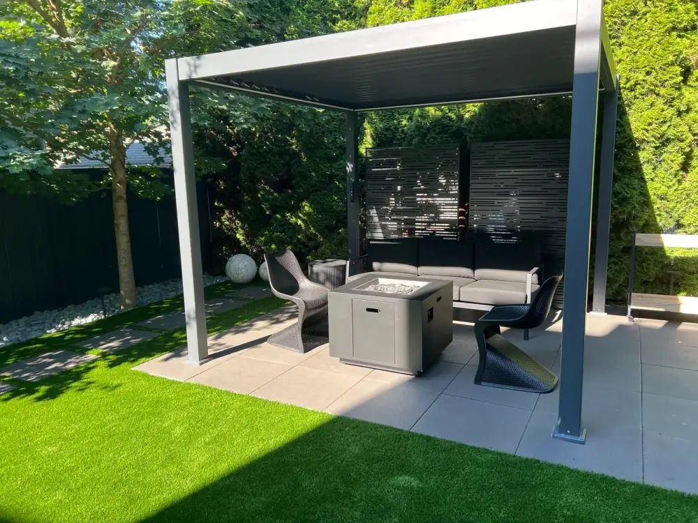 Modern aluminium pergola over an outdoor lounge with a fire table, beside an artificial turf lawn