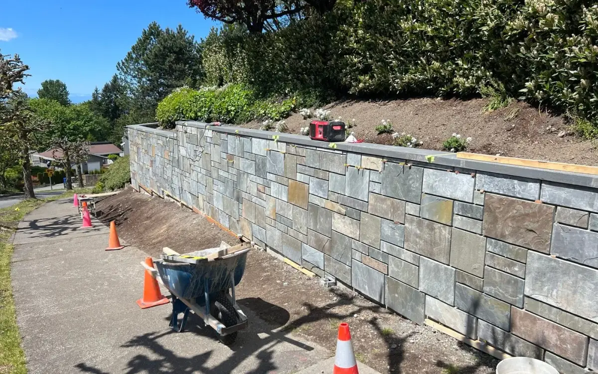 Natural stone veneer retaining wall under construction with tools and materials on site